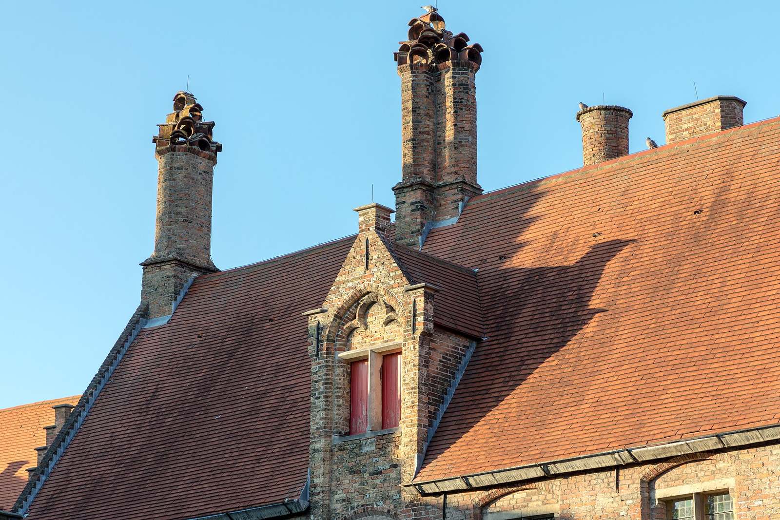 Historisch gebouw met een rood pannendak, een trapgevel en schoorstenen in Brugge